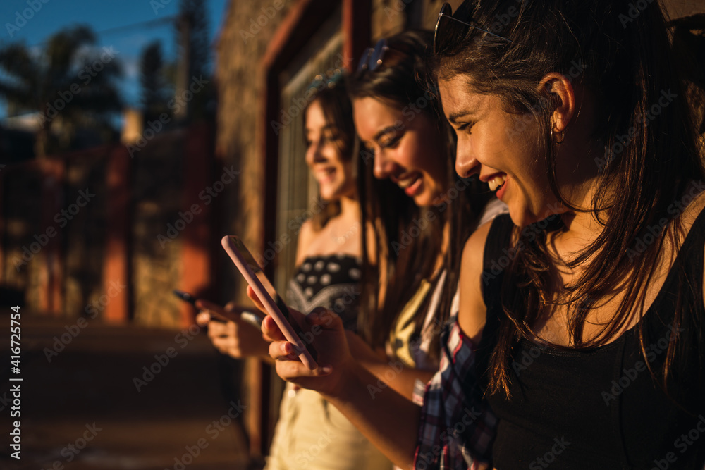 Obraz premium Three girls chatting with their smartphones at the park.