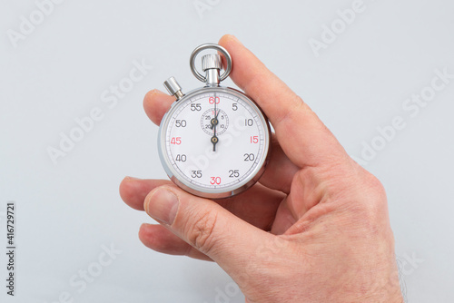 Man holding analog stopwatch on the gray background.