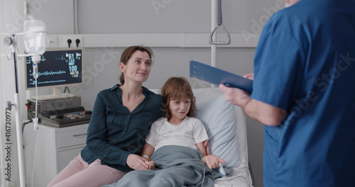 Aged male doctor discussing treatment with kid patient and mother in ward at hospital.