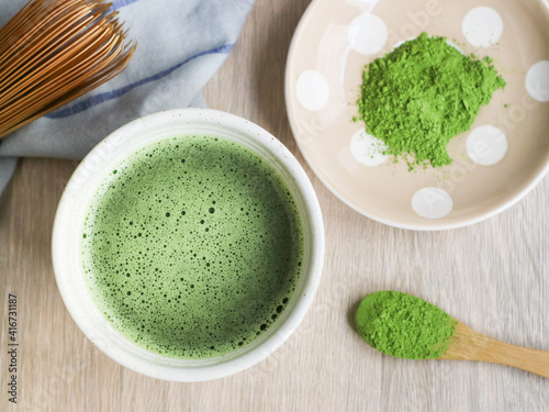 Top view of a bowl of traditional Japanese matcha green tea with its powder and chesen whisk on a wooden table, a healthy antioxidant concept 