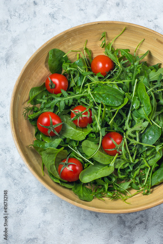 Spinach and arugula salad with tomatoes in a large bowl on a light background top view vertical arrangement