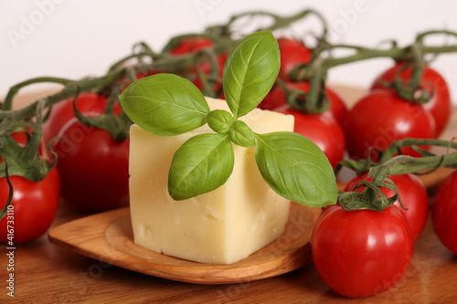 Ein Stück Käse mit Holzlöffel auf einem Holzbrett und Tomaten, Basilikum