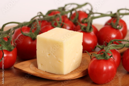 Ein Stück Käse mit Holzlöffel auf einem Holzbrett und Tomaten