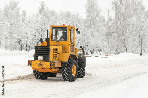 A large yellow tractor of the municipal service clears snow on city streets russia