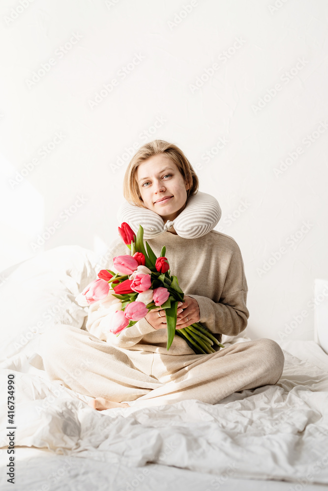 Sleepy woman sitting in bed wearing pajamas and pillow over the neck