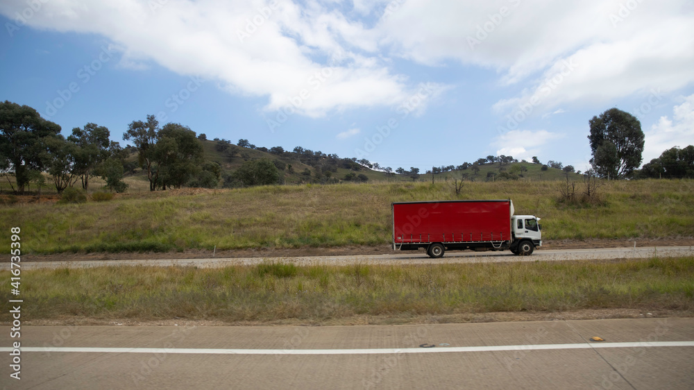 Truck on a freeway with plane flying overhead in Australian Country Town midway between Sydney and Melbourne with nice blue sky and lush green trees as a backdrop Truck on a freeway with plane flying overhead in Australian Country Town midway between Sydney and Melbourne with nice blue sky and lush green trees as a backdrop