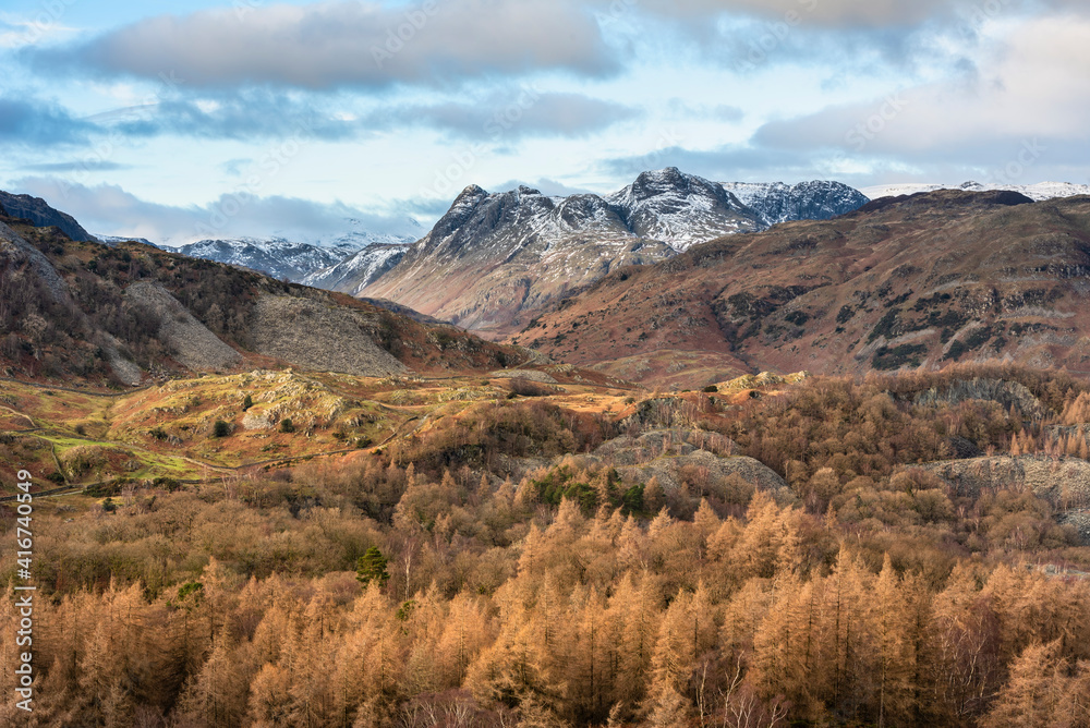 Majestic Winter landscape image view from Holme Fell in Lake District towards snow capped mountain ranges in distance in glorious evening light with Autumnal colors trees