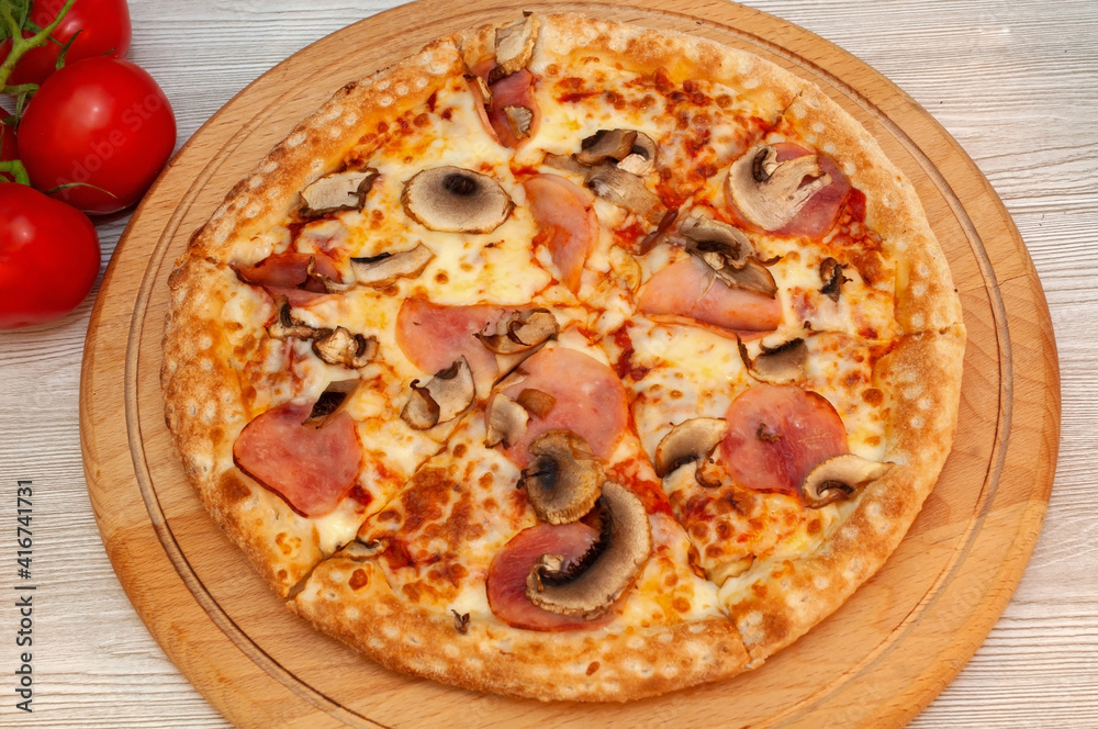 Pizza with ham, mushrooms and cheese on a board with tomatoes