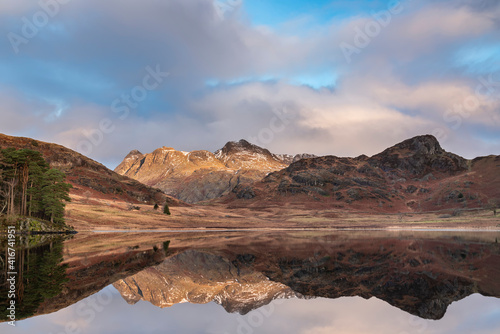 Beautiful vibrant Winter sunrise over Blea Tarn in Lake District with snow capped Langdale Pikes in distance © veneratio