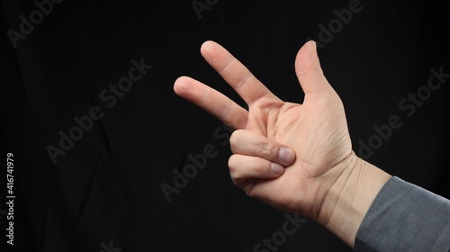 Men's hand gesturing, gesture, enumeration three, three fingers, isolated black background. Emotion