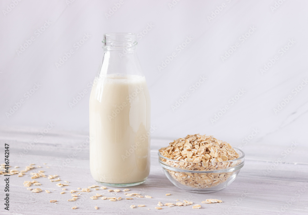 Vegetable oat milk in a glass bottle and oat flakes on a light background. Healthy drinks, vegetarianism. Side view Vegetable oat milk in a glass bottle and oat flakes on a light background. Healthy drinks, vegetarianism. Side view