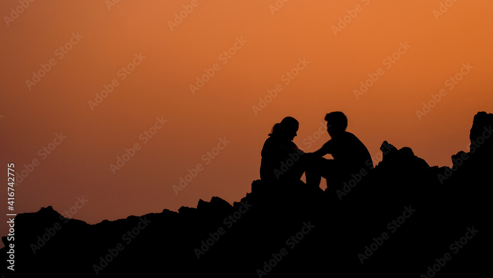 A couple sitting on the rock silhouette