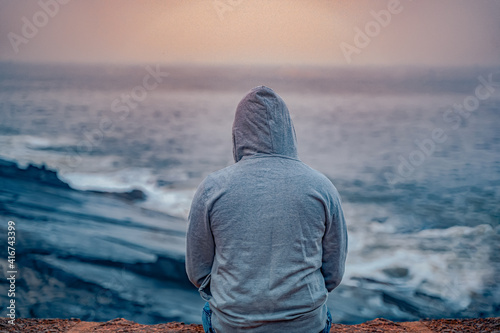 Canvas Print Anonymous guy sitting near seashore wearing grey hoodie