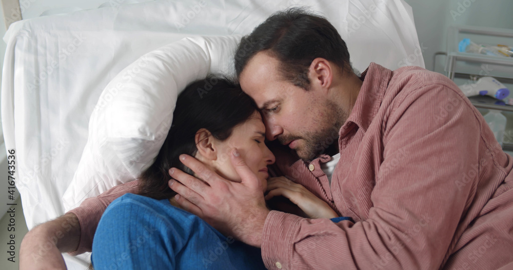 Husband hugging and comforting crying sick woman lying together in hospital bed Husband hugging and comforting crying sick woman lying together in hospital bed
