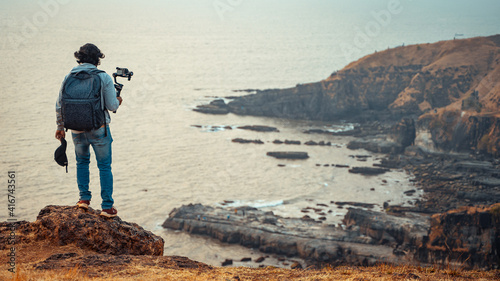 Photos Independent filmmaker standing on the cliff holding camera in his hand