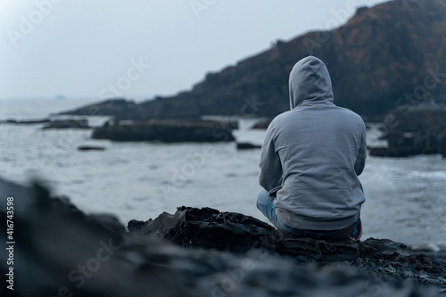 Photography An anonymous man sitting near seashore wearing a grey hoodie