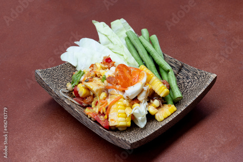 Beside view of Food of Thailand Spicy Salad name of Thai Som Tam Kai Kem with Khow Phod. Papaya Salad with Corn and Salted Egg. Set up and serve on a coconut plate. brown tile floor as a background. photo