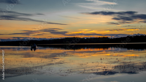 Two people are sailing in a boat. Beautiful sunset landscape over a Finnish lake. The space is flooded with gold.
