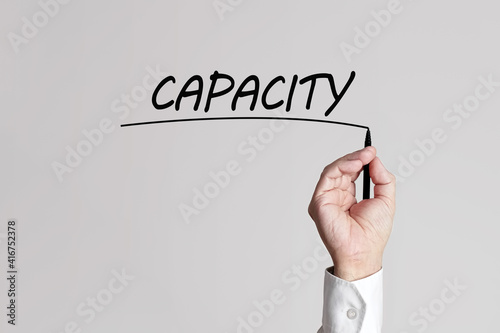 Businessman hand with pen underlines the word capacity on a gray background virtual screen.