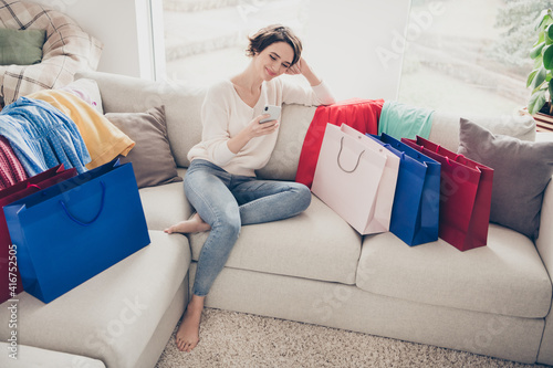 Full size photo of brunette bob haired lady sit couch look use phone smile shopping bags indoors in house © deagreez