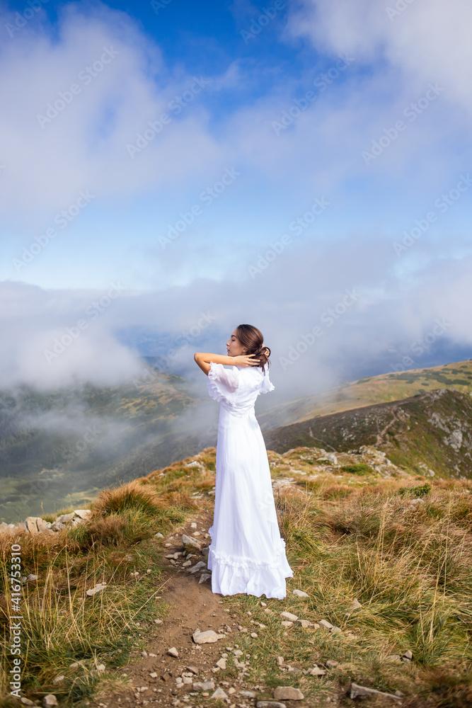 young woman in a white dress high in the mountains in the clouds