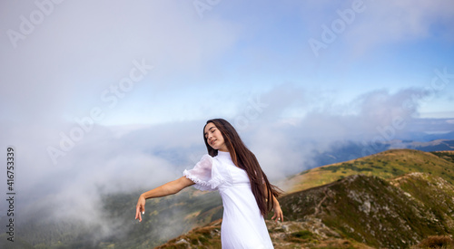 young woman in a white dress high in the mountains in the clouds