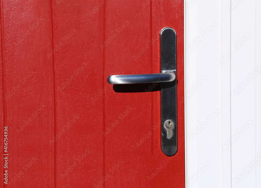 A closeup view of a grey brushed chrome handle on a red door. A closeup view of a grey brushed chrome handle on a red door.