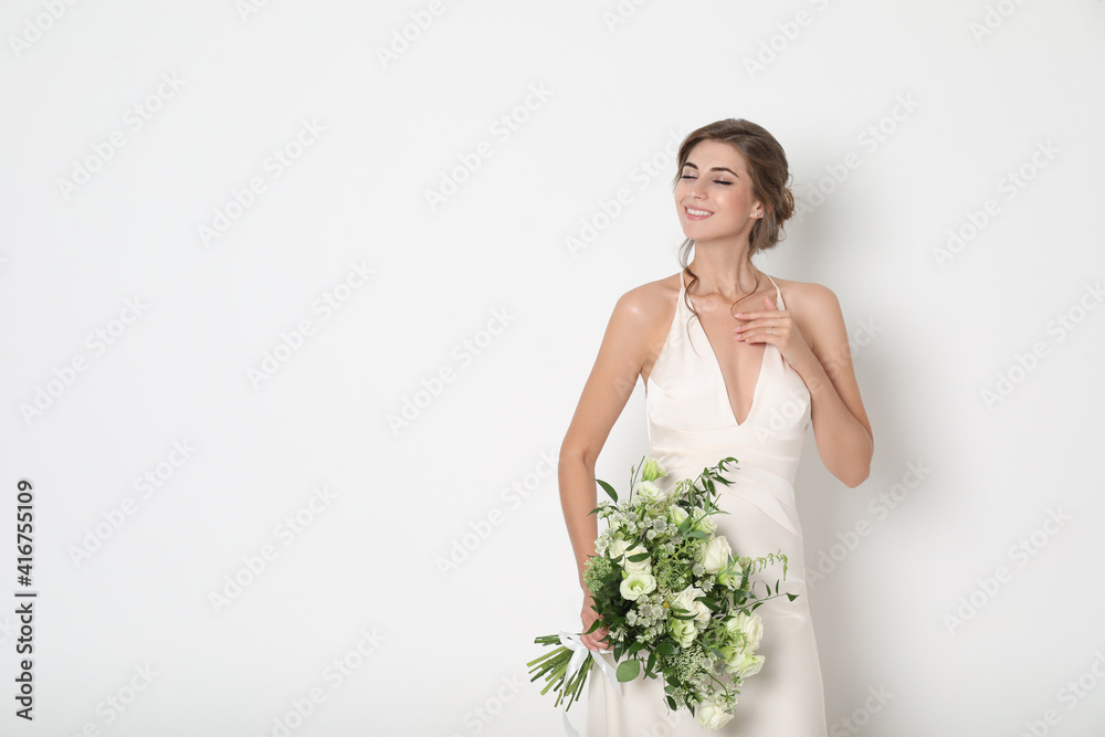 Young bride wearing wedding dress with beautiful bouquet on light background. Space for text Young bride wearing wedding dress with beautiful bouquet on light background. Space for text