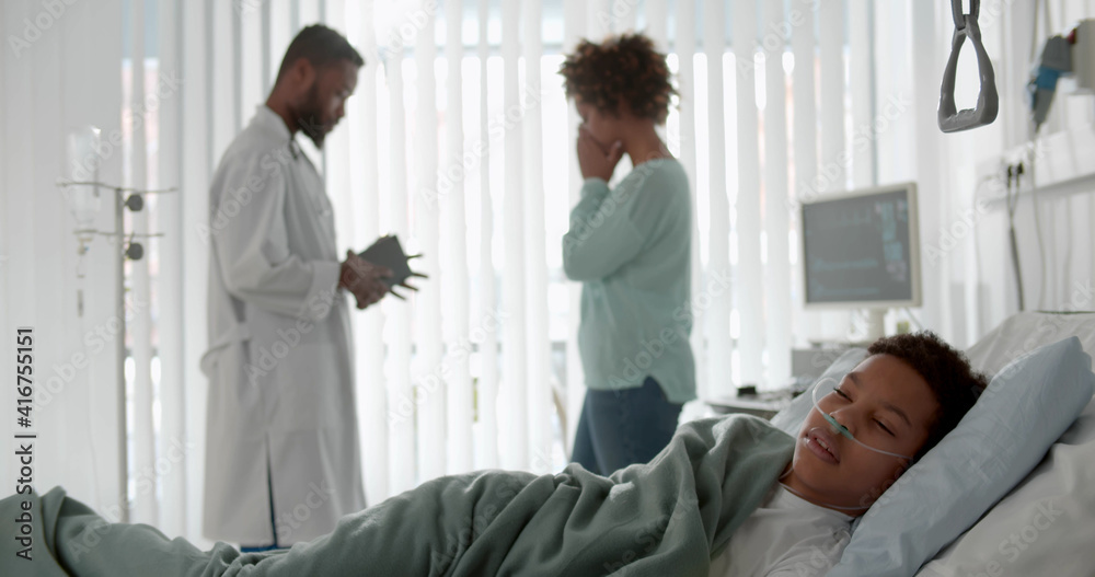 Obraz premium African sick kid sleeping in hospital bed with doctor telling mother bad news on background