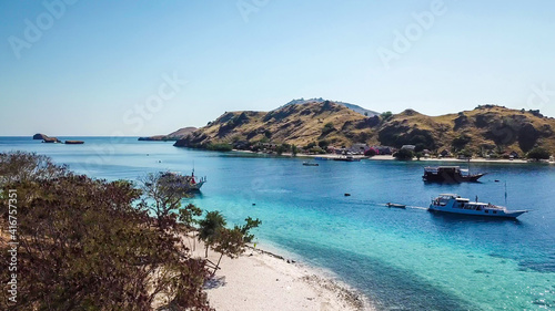Top down drone shot of a paradise island with some boats anchored around in Komodo National Park, Flores, Indonesia. Brownish island turns into white sand beach and further into green and navy sea © Chris