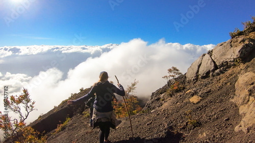 A young woman walking down the volcano Inierie in Bajawa, Flores, Indonesia. She supports herself on a wooden stick while enjoying the beautiful view on volcanic island. Lots of fluffy clouds around photo