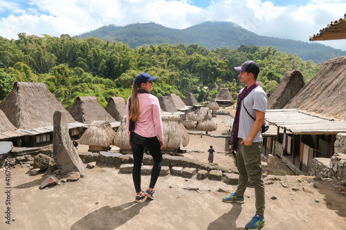 A couple with a purple scarfs admiring the Beno village in Flores, Indonesia. There are many small houses behind him. Each house is made of natural parts like wood and straw. History and tradition photo