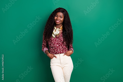 Photo of shiny sweet curly dark skin woman dressed red shirt standing arms pockets isolated green color background
