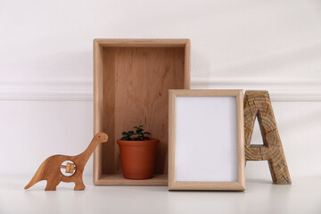 Empty photo frame, cute toy dinosaur, wooden letter and crate with houseplant near wall, space for text. Baby room interior element