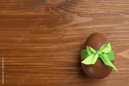 Sweet chocolate egg with green bow on wooden table, top view. Space for text