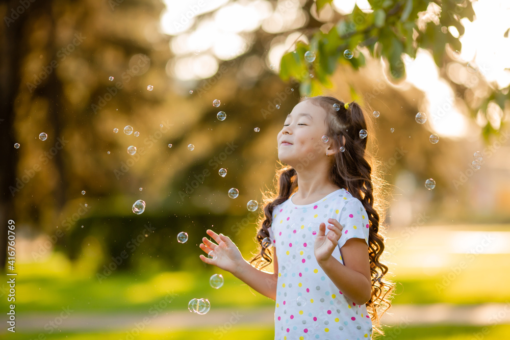 Cute little Asian girl in the summer on a walk blowing soap bubbles Cute little Asian girl in the summer on a walk blowing soap bubbles