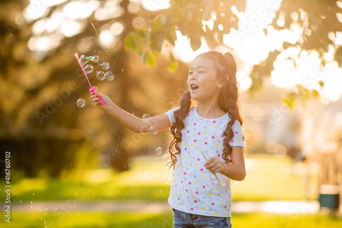 Cute little Asian girl in the summer on a walk blowing soap bubbles