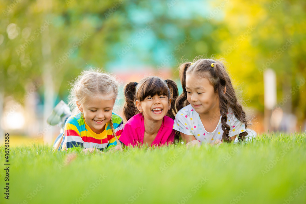 Three little girls of Asian, Indian and European ethnic predation lie on the lawn in the summer. International Children's Day Three little girls of Asian, Indian and European ethnic predation lie on the lawn in the summer. International Children's Day