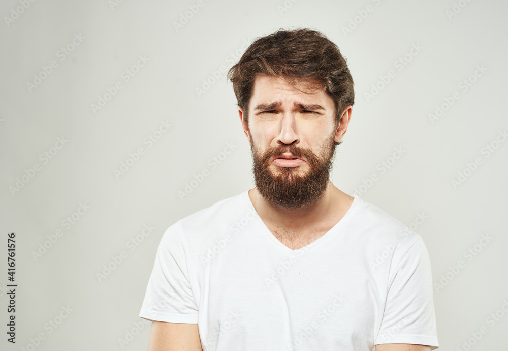 Nice guy with a beard in a white T-shirt on a light background cropped view of a sad face Nice guy with a beard in a white T-shirt on a light background cropped view of a sad face