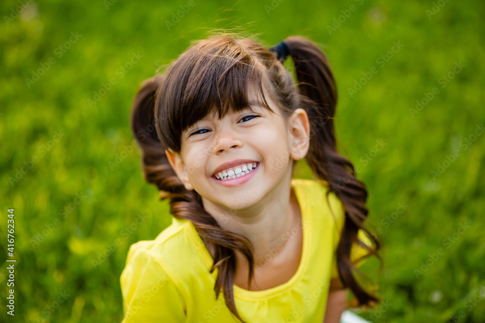 Happy little Indian girl in yellow T-shirt laughs summer on the lawn