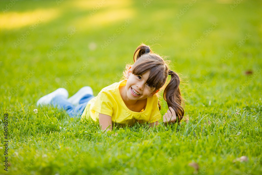 Fototapeta premium Happy little Indian girl in yellow T-shirt laughs summer on the lawn