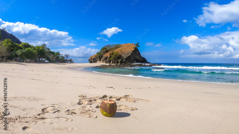 A fresh coconut juice in a coconut shell in the middle of an empty, idyllic Koka Beach. Hidden gem of Flores, Indonesia. Island life. Beach gently washes by calm waves. Simplicity and healthy diet. A fresh coconut juice in a coconut shell in the middle of an empty, idyllic Koka Beach. Hidden gem of Flores, Indonesia. Island life. Beach gently washes by calm waves. Simplicity and healthy diet.