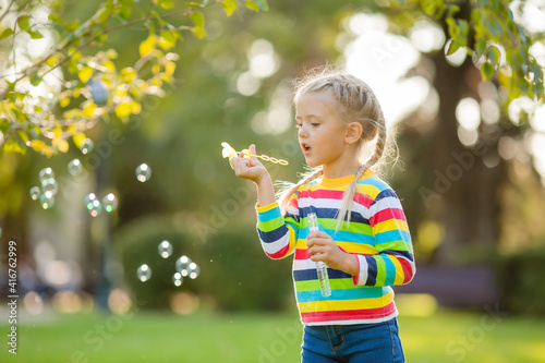 Cute little girl on a walk in a multi-colored knitted blouse in a striped summer blowing soap bubbles