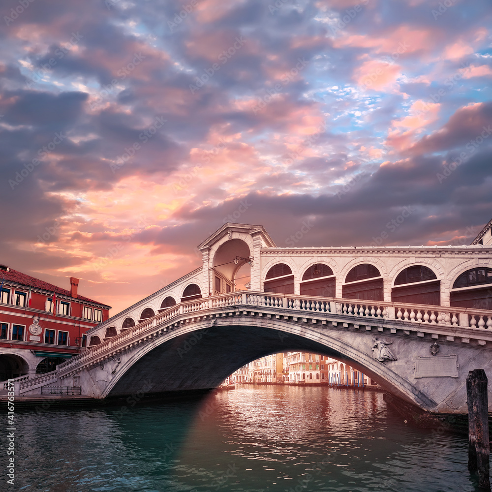 Rialto bridge on The Grand Canal in Venice, Italy in the evening on sunset. Pink purple sky with clouds.Toned square image. Famous place, romantic sights of Venice in Italy.