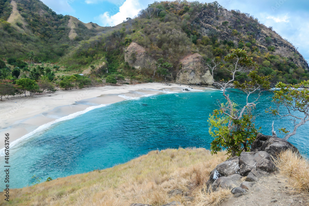A view on idyllic Koka Beach from a nearby headland. Hidden gem of Flores, Indonesia. Beach is gently washed by waves. Serenity and calmness. Island life. Beach surrounded by mountains.