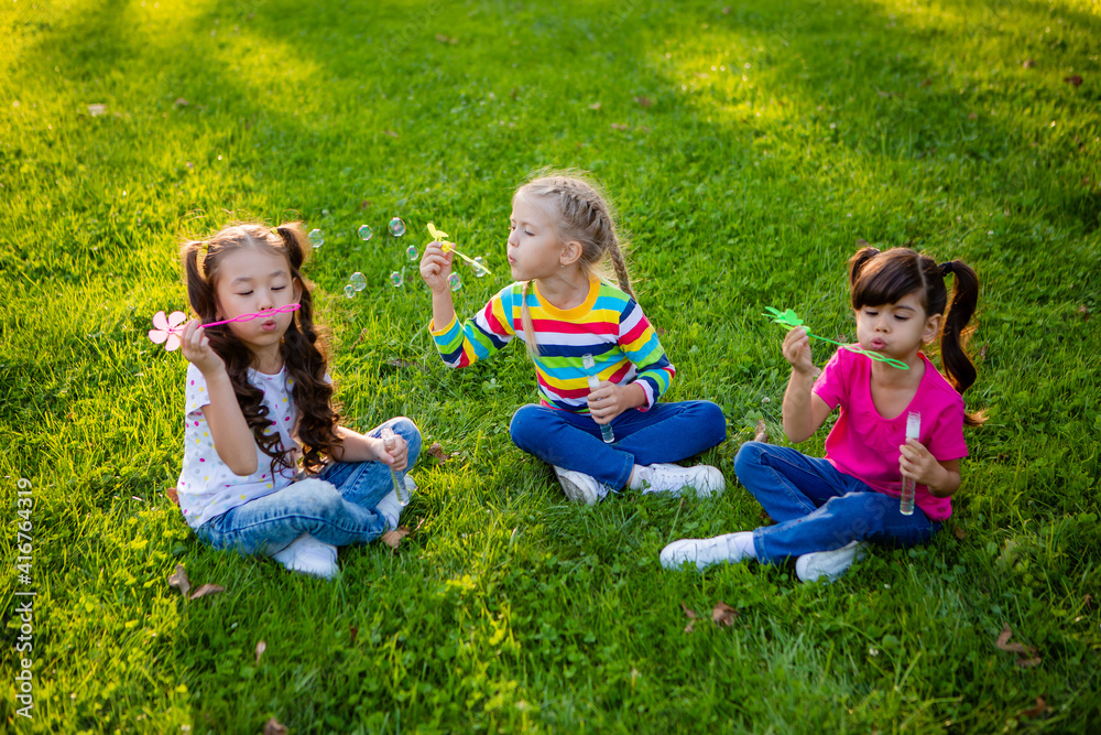 three little girls of European, Indian and Asian ethnicity in the summer blow soap bubbles. International Children's Day three little girls of European, Indian and Asian ethnicity in the summer blow soap bubbles. International Children's Day