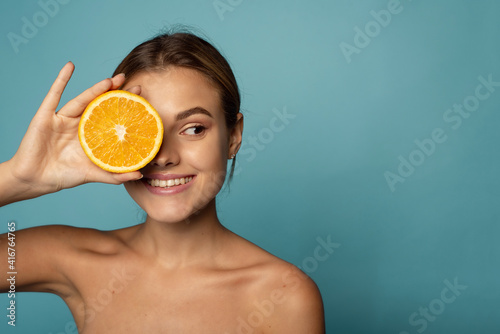 Attractive caucasian female with clean skin laughing with closed eyes and showing half of fresh orange while advertising benefits of vitamin C photo