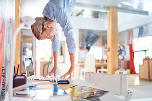 Hard work concept. Technology and business. Young woman hanging upside down over desktop.