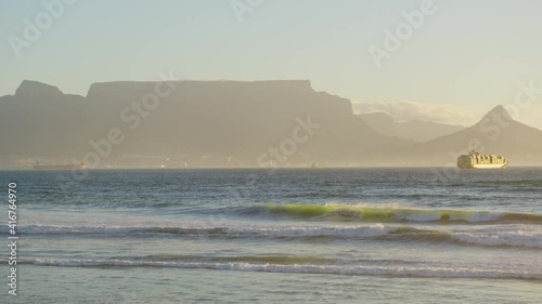 Beautiful clear day looking to table mountain and mother city with ocean waves crashing over rocky shore line.
