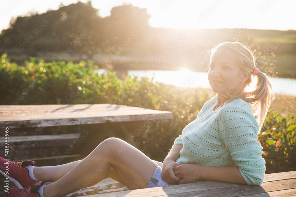 blonde girl in shorts sitting at sunset at the wooden table near the lake